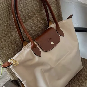 Foto casera de un bolso beige con asas de piel café, apoyado en una silla