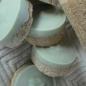 Foto casera de jabones verdes con esponja de estropajo sobre una toalla blanca
